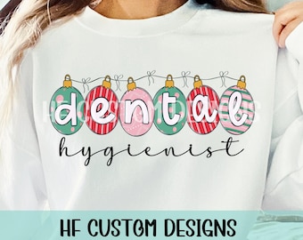 May include: White sweatshirt with a Christmas ornament design that spells out "dental hygienist".