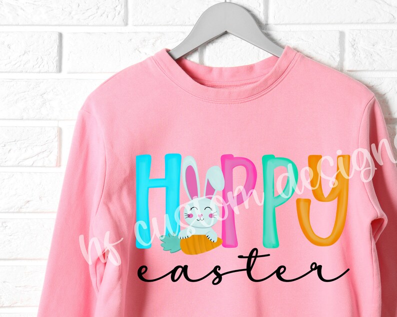 May include: Pink sweatshirt with the text "Happy Easter" in colorful letters. A cartoon bunny holding a carrot is in the middle of the word "Happy".