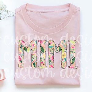 Pu&ograve; includere: Maglietta rosa con la parola "MIMI" in grandi lettere contornate. Le lettere sono riempite con un motivo floreale in tonalit&agrave; rosa, giallo, verde e bianco.