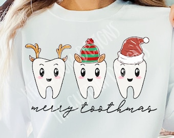 May include: White sweatshirt with a Christmas-themed design featuring three cartoon teeth wearing festive hats. The teeth have reindeer antlers, a striped elf hat, and a Santa hat. The text "merry toothmas" is printed below the teeth.