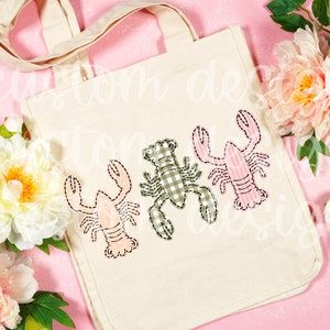 May include: A white canvas tote bag with three embroidered lobsters. The lobsters are in different colors and patterns: pink with white stripes, green with white gingham, and pink with white polka dots.