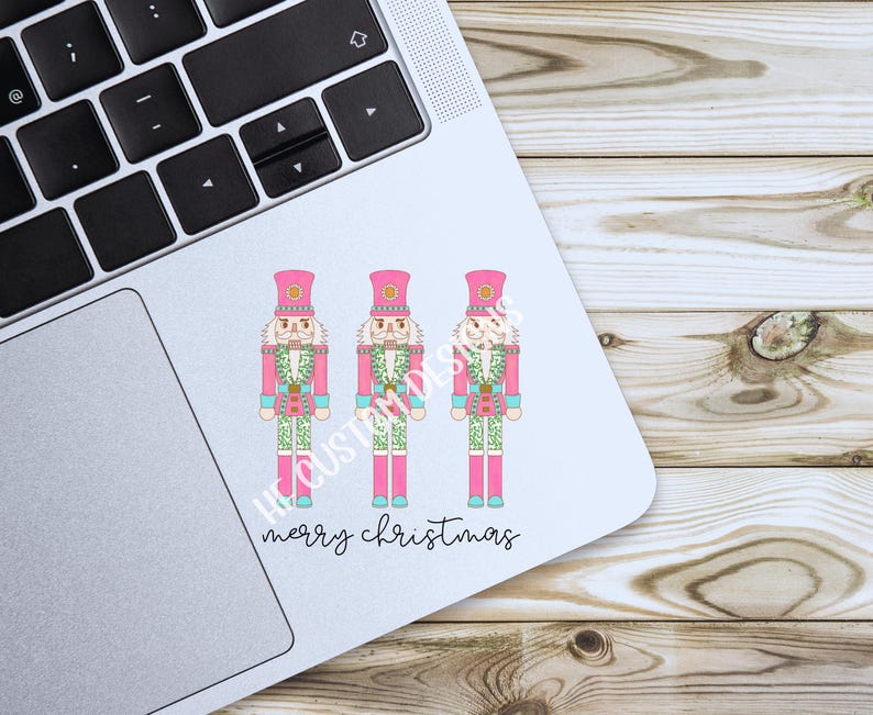 May include: Three pink nutcracker figurines with green and white accents stand in a row on a white background. The text "merry christmas" is written below the figurines.