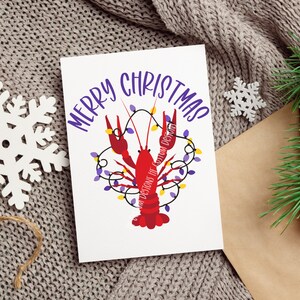 May include: A white card with the text "Merry Christmas" in purple lettering. A red crawfish with purple and yellow lights is illustrated on the card.