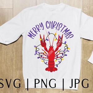 May include: White long-sleeved sweatshirt with the text "Merry Christmas" in purple lettering. A red crawfish with purple and yellow Christmas lights is in the center of the shirt.