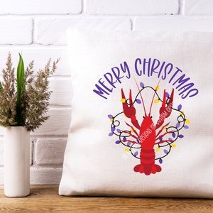 May include: A white pillow with the text "Merry Christmas" in purple lettering. A red crawfish is decorated with purple and yellow lights.