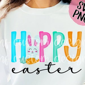 May include: A white sweatshirt with the text "Happy Easter" in colorful letters. A cartoon bunny holding a carrot is in the middle of the word "Happy".