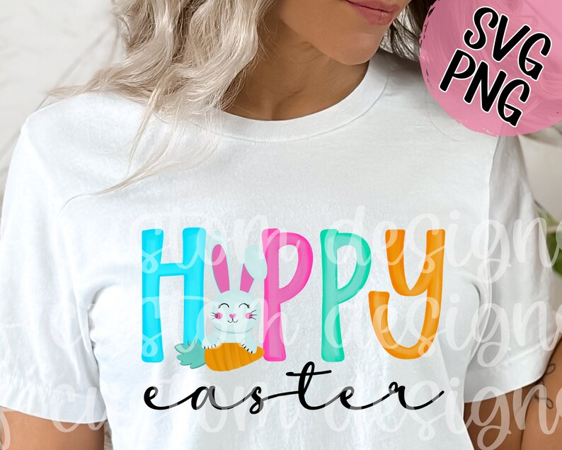 May include: White t-shirt with the text "Happy Easter" in colorful letters. A cartoon bunny holding a carrot is in the middle of the word "Happy".