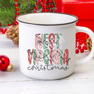 May include: White ceramic mug with a black rim. The mug has a festive design with the text "West Virginia Christmas" in pink, green, and red lettering with string lights.