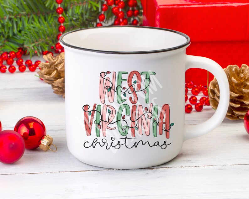 May include: White ceramic mug with a black rim. The mug has a festive design with the text "West Virginia Christmas" in pink, green, and red lettering with string lights.