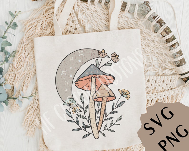 May include: A tote bag with a design of two mushrooms with orange and pink caps, a crescent moon with stars, and floral accents. The design is in a boho style.