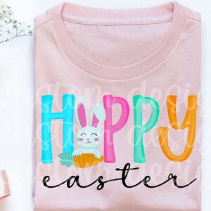 May include: A pink t-shirt with the text "Happy Easter" in colorful letters. A white bunny holding a carrot is in the middle of the word "Happy".