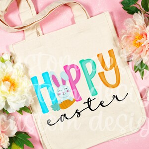 May include: A white canvas tote bag with a colorful "Happy Easter" design featuring a cartoon bunny holding a carrot. The letters are in different colors and the word "Easter" is in a cursive font.