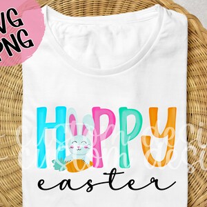 May include: White t-shirt with the text "Happy Easter" in colorful letters. A cartoon bunny holding a carrot is in the middle of the text.