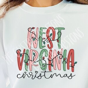May include: White sweatshirt with a festive design that says "West Virginia Christmas" in colorful, outlined letters with red, green, and pink accents. The letters are decorated with a string of lights.