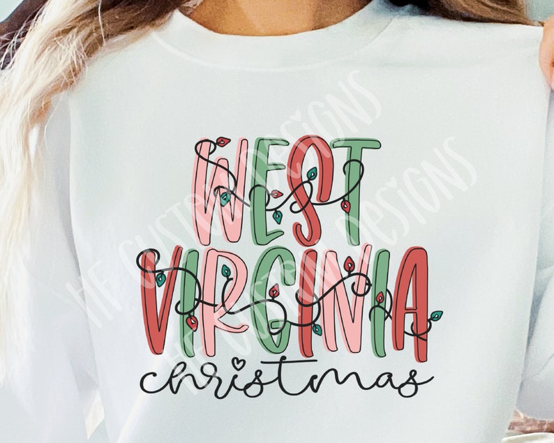 May include: White sweatshirt with a festive design that says "West Virginia Christmas" in colorful, outlined letters with red, green, and pink accents. The letters are decorated with a string of lights.