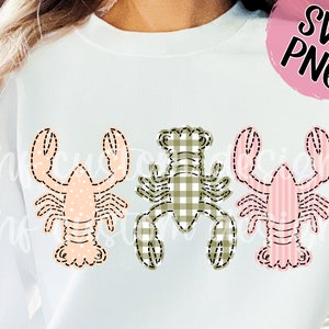 May include: Three embroidered lobster designs on a white sweatshirt. The lobsters are in different patterns: pink with white polka dots, green and white gingham, and pink and white stripes.