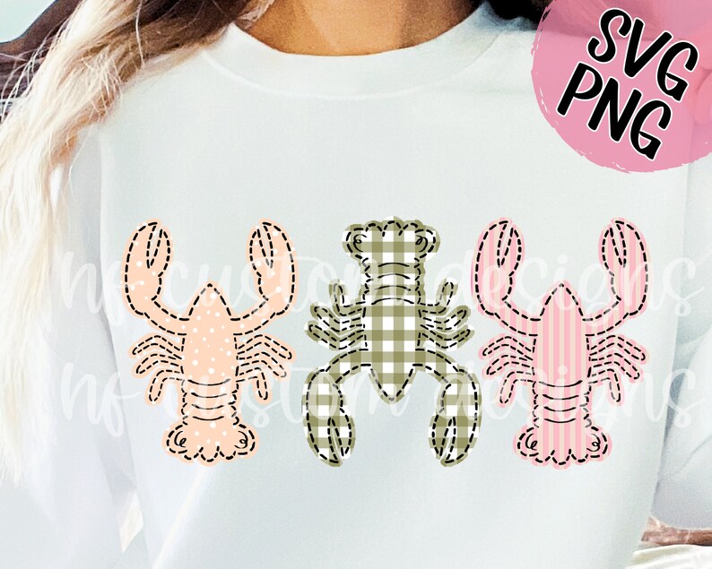 May include: Three embroidered lobster designs on a white sweatshirt. The lobsters are in different patterns: pink with white polka dots, green and white gingham, and pink and white stripes.