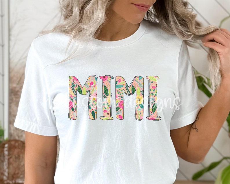 Pu&ograve; includere: Maglietta bianca con la parola "MIMI" in grandi lettere rosa bordate di nero. Le lettere sono riempite con un motivo floreale in tonalit&agrave; rosa, verde e giallo.