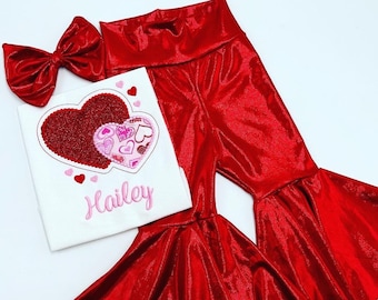 May include: Red glitter bell bottom pants with a white shirt featuring a pink and red heart design and the name Hailey embroidered on the shirt.