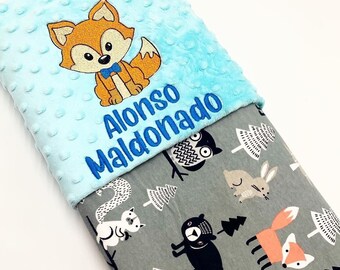 May include: A light blue baby blanket with a white and black woodland animal print on the reverse side. The blanket features a fox with a blue bow tie and the name "Alonso Maldonado" embroidered on the front.