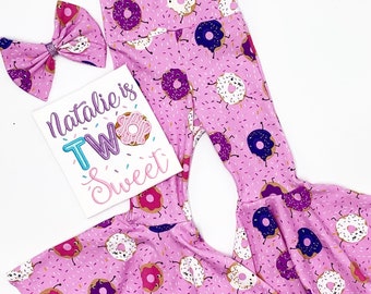 May include: Pink and white donut print bell bottom pants with a white shirt that says "Natalie is Two Sweet" and a pink and white donut print bow.