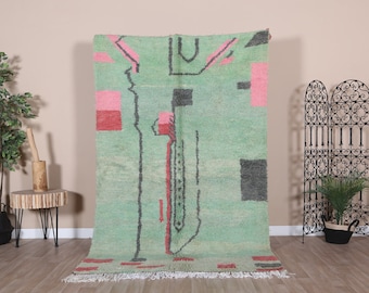 May include: A green, pink and black abstract rug with a geometric design. The rug has a fringe border and is made of wool.