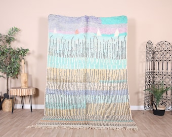 May include: A colourful handwoven rug with a geometric pattern in shades of blue, green, yellow, and white. The rug has a fringe border and is made of wool.