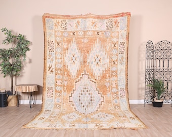 May include: A vintage Moroccan rug with a beige background and intricate patterns in shades of brown, pink, and blue. The rug has a distressed look and is woven with a variety of textures.
