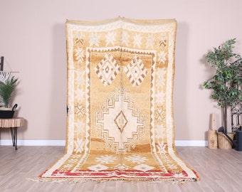 May include: A large, rectangular, handwoven rug with a beige background and intricate white geometric patterns. The rug has a red and white border.