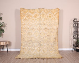 May include: A large, rectangular rug with a geometric diamond pattern in shades of yellow and cream. The rug is hanging on a wall, showcasing its size and design. The rug has a fringed edge.