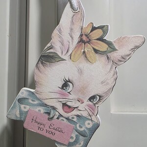 May include: Vintage Easter bunny decoration with a floral accent and a blue bow tie. The bunny has a pink nose and cheeks, and the text "Happy Easter TO YOU" is on a pink tag.