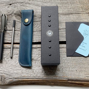 May include: A blue leather pen case, a silver pen, a silver mechanical pencil, a black box with a silver logo, and a blue card with the text "Welcome to the team, Emma!" in a black envelope.