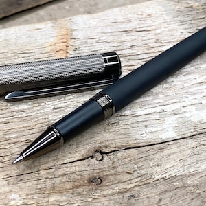 May include: A black and silver retractable pen with a textured barrel and a silver clip. The pen is lying on a wooden surface.