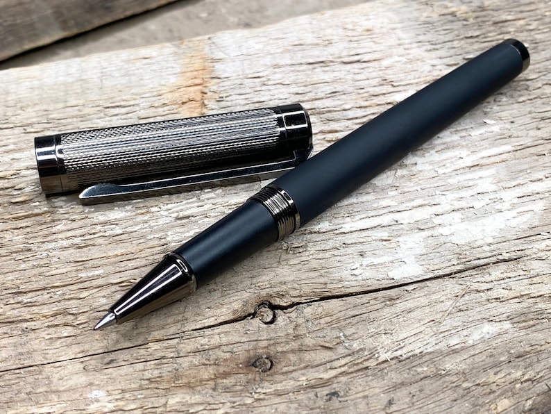 May include: A black and silver retractable pen with a textured barrel and a silver clip. The pen is lying on a wooden surface.