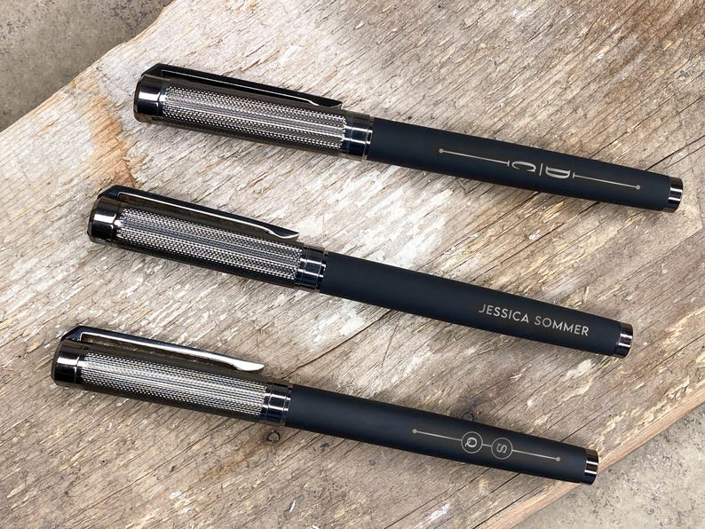 May include: Three black pens with silver accents and engraved names. The pens have a textured metal barrel and a black clip.