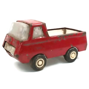 May include: A vintage red toy truck with a clear windshield and white interior. The truck has black tires with white centers and shows signs of wear and rust. The toy truck is a classic collectible.