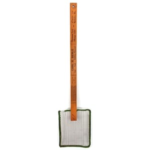 May include: A vintage fly swatter with a wooden handle and a square mesh head. The handle has printed text including "CARL H. BEHLE" and "Floriunst Yard". The mesh head is white with black lines and a green border.
