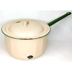 May include: Cream-colored enamelware pot with a lid and a long green handle. The pot has a green trim around the rim and on the handle. The lid has a small handle. The pot appears to be vintage or antique.