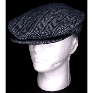 May include: A dark blue and gray herringbone pattern newsboy cap. The cap is displayed on a white foam head against a black background. The cap has a rounded crown and a small, stiff brim.