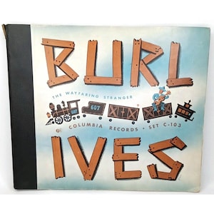 May include: A vintage Columbia Records album cover for Burl Ives, The Wayfaring Stranger, Set C-103. The cover features large, brown, wood-plank style lettering for the name Burl Ives, with a graphic of a steam train and a musician playing guitar.
