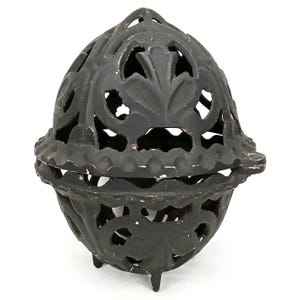 May include: A black, cast iron incense burner with a decorative, openwork design. The burner is egg-shaped, with a hinged lid and three small feet. The intricate pattern includes floral and geometric shapes, and the finish has some wear.