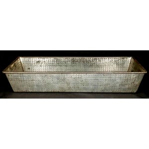 May include: A rectangular, galvanized metal baking pan with a textured surface. The pan has slightly sloped sides and a rectangular shape. The word "BROWNE" is embossed on the front of the pan. The pan is a light gray color.