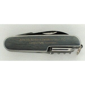May include: A silver multi-tool pocket knife with a brushed metal finish. The knife has a variety of tools, including a blade, a screwdriver, and a bottle opener. The knife is engraved with the text "Arnold, Behrens, Deters & Gray, P.C. Certified Public Accountants."