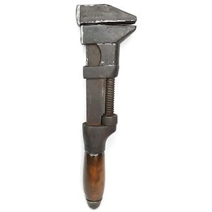 May include: A vintage adjustable wrench featuring a dark, weathered metal head and a threaded adjustment screw mechanism. The tool includes a smooth, rounded wooden handle with a polished brown finish, attached to the metal shaft base.