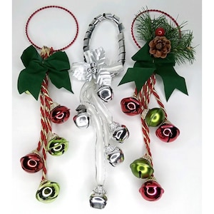 May include: Three hanging holiday ornaments featuring circular frames. The left and right ornaments have green bows, pine needles, pinecones, and red and green jingle bells on gold-trimmed red cords. The center ornament has silver ribbons and bells.
