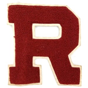 May include: A vintage red letter "R" patch with a white border. The letter has a textured, felt-like appearance. This patch is likely for a varsity jacket or other apparel, and is a classic piece of collegiate or team memorabilia.