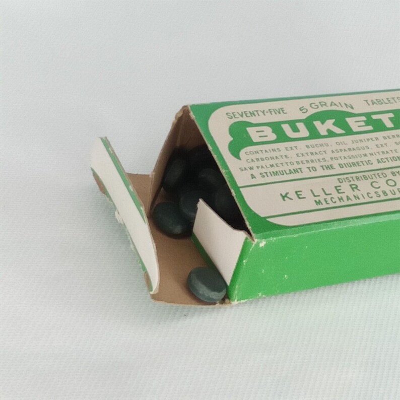 K&ouml;nnte beinhalten: Eine gr&uuml;ne Schachtel mit Buket 5-Korn-Tabletten, mit einem wei&szlig;en Etikett, auf dem "SEVENTY-FIVE 5 GRAIN TABLETS" und "BUKET" steht. Die Schachtel ist ge&ouml;ffnet und die gr&uuml;nen Tabletten sind im Inneren sichtbar.