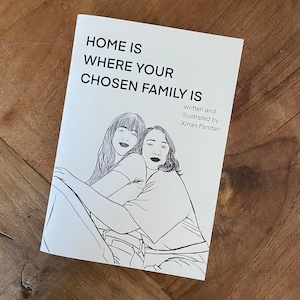 May include: Book cover with the title "Home is Where Your Chosen Family Is" written in black text. The cover features a black and white illustration of two women hugging.