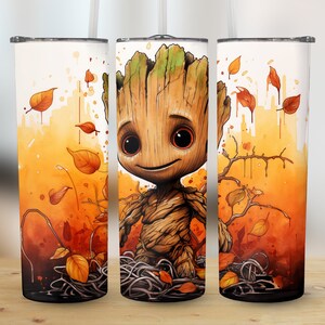 Könnte beinhalten: Ein weißer Becher mit einer Aquarellillustration einer Groot-ähnlichen Figur, umgeben von Herbstblättern. Das Design verwendet Orange-, Braun- und Grüntöne, mit Strohhalm und Deckel. Der Becher ist für kalte Getränke konzipiert.