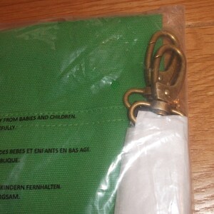 Puede incluir: Una bolsa de lona verde con un cierre de lat&oacute;n. La bolsa tiene una etiqueta de advertencia que dice: "Mantener fuera del alcance de beb&eacute;s y ni&ntilde;os. Manipular con cuidado."